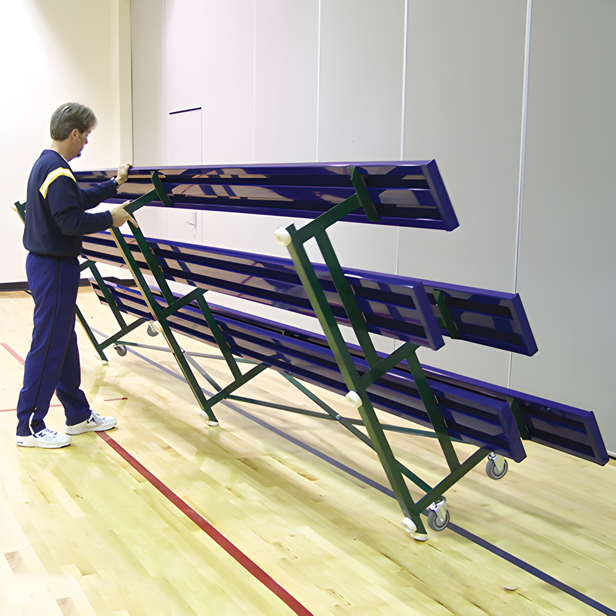 Man folding indoor bleacher seats with green frame and wheels.