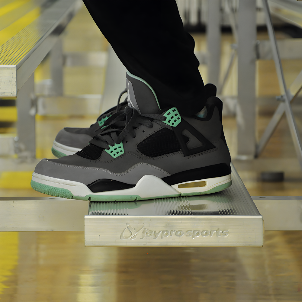 Person wearing black and green sneakers standing on metal bleachers.