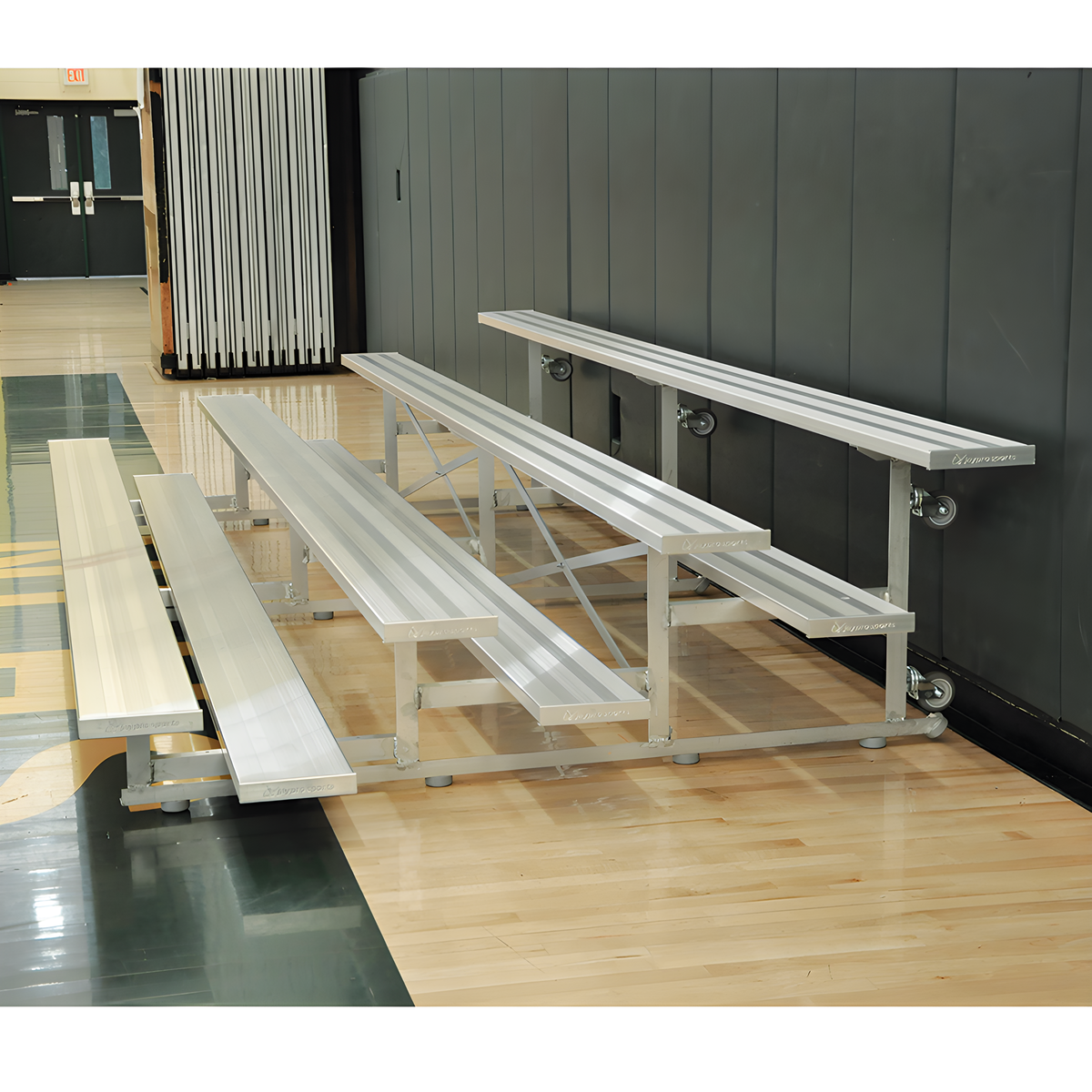 Silver aluminum bleachers with wheels in indoor gymnasium with blue padding.