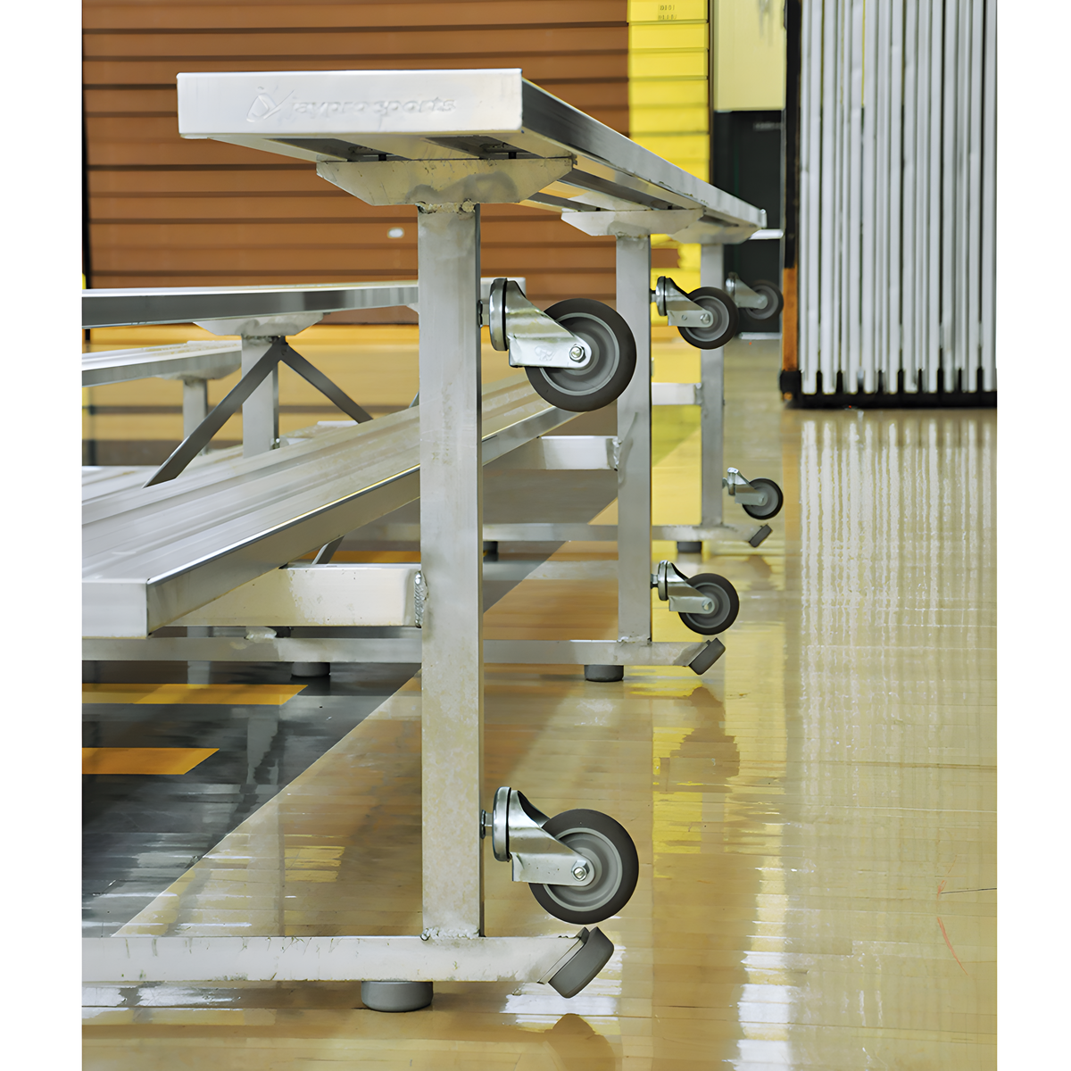 Close-up of aluminum bleachers with wheels on polished gym floor.