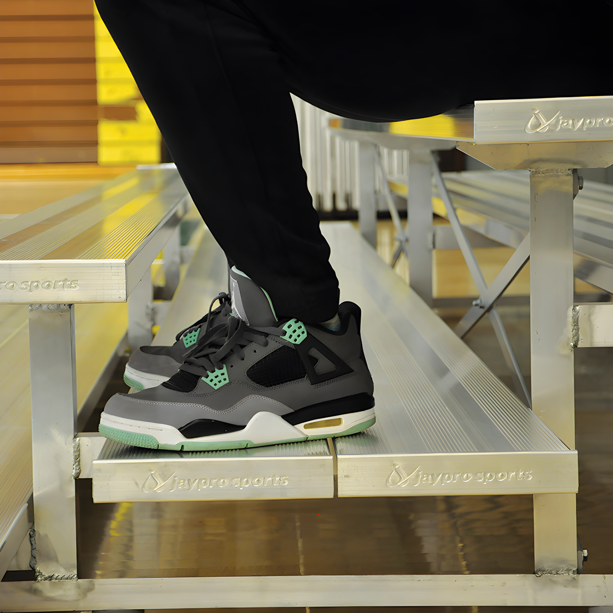 Person wearing sneakers sitting on indoor bleacher seats with aluminum frame.