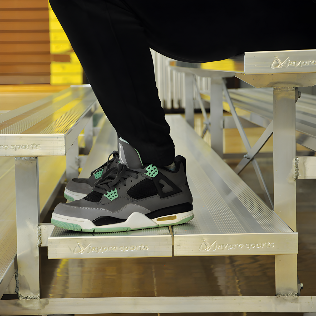 Close-up of person wearing sneakers sitting on aluminum bleachers.