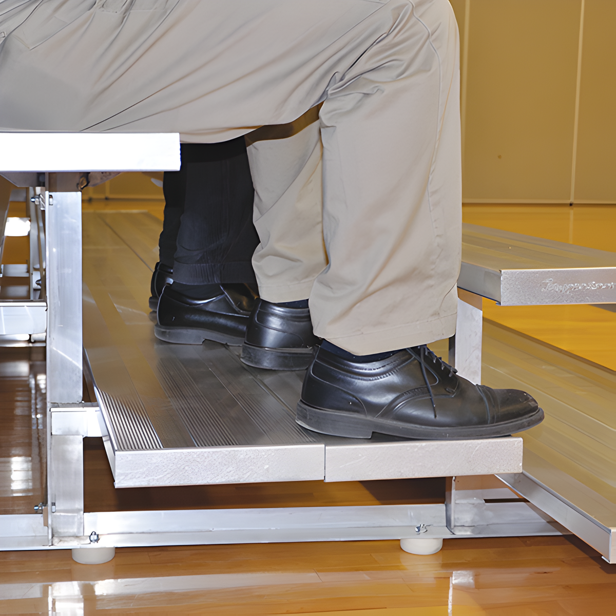 Person wearing sneakers sitting on indoor bleacher seats with aluminum frame.