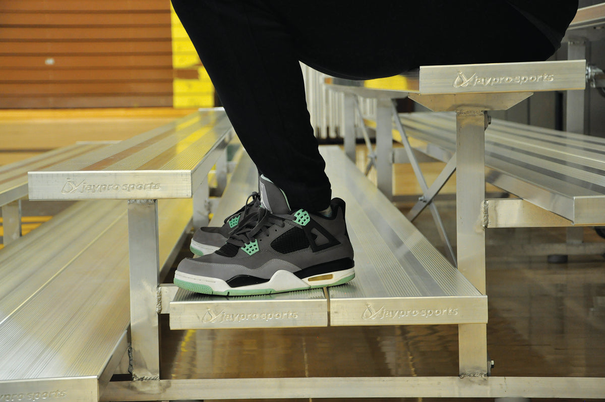 Person wearing sneakers sitting on indoor bleacher seats with aluminum frame.