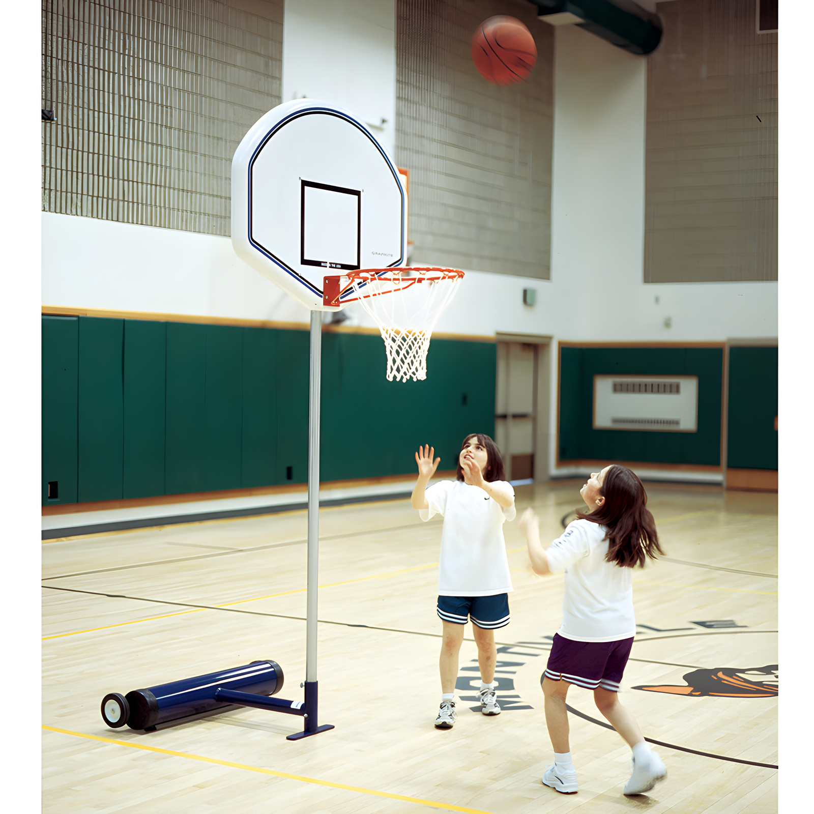 Two young girls playing basketball in a school gymnasium.