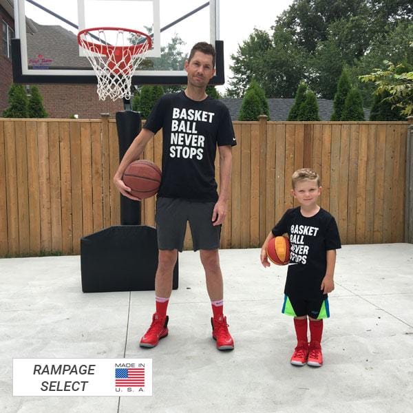 a father and son holding basketball balls and portable basketball goal at the back of them 